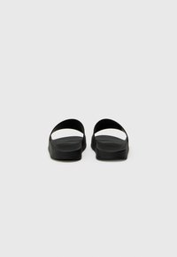 Black slide sandals featuring a minimalistic design, flat soles, and two wide straps with a smooth texture. No visible hardware or patterns.