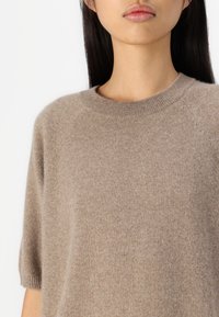 Beige kasjmier trui met korte mouwen, ronde halslijn en een zachte textuur. Heeft een relaxte pasvorm en subtiele raglannaaddetails.