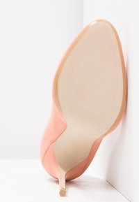 Chaussure à talon aiguille rose corail avec un bout pointu et une surface en daim lisse. La semelle est beige avec un motif texturé pour une meilleure adhérence.