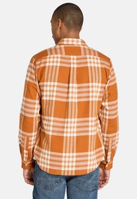 Camisa de franela a cuadros en naranja y crema con collar abotonado, mangas largas y dobladillo recto. Fabricada en un tejido suave y texturizado.
