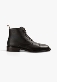 Bota de tobillo de cuero negro con superficie texturada, puntera redondeada y detalles en la punta. Presenta cordones en la parte frontal y una tira en la parte trasera para facilitar el calzado.