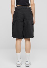 Sorte cargo shorts laget av denim. Avslappet passform med sidelommer, baklommer med lapp, og oppbrett nederst. Brukt med hvite joggesko og sokker.