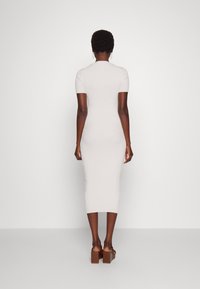 Strick-Midi-Kleid in hellbeige, figurbetontes Design mit kurzen Ärmeln, gerippter Textur und geradem Saum, getragen mit braunen Plateausandalen.