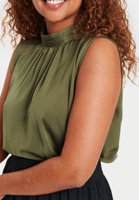 Olive green sleeveless blouse with pleated detailing at the collar, paired with a black waistband. Smooth, lightweight fabric texture.