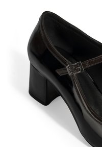 Schwarzer Lackleder-Hochschuh mit einem quadratischen Absatz, ausgestattet mit einem dünnen Riemen und einer kleinen Schnallenverzierung. Glatte Oberfläche, runde Zehenform.