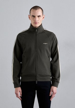 Giacca zip-up verde scuro in pile con strisce bianche sui lati. Presenta un colletto alto e tasche anteriori con zip.