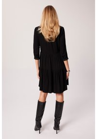 Czarna sukienka do kolan z rękawami trzyczworć, marszczonymi tierami i dekoracyjnymi guzikami na rękawach. Gładka tekstura materiału.