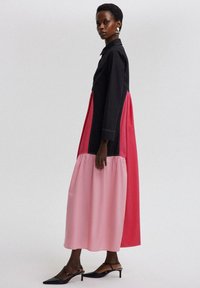 Pitkä mekko, jossa on musta farkkubodice, kirkkaat vaaleanpunaiset ja punaiset kerrokset sekä hulmuava helma. Tyylikkäät, terävät mustat korkokengät täydentävät asua.