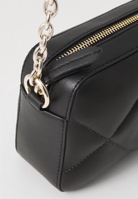 Svart läderhandväska med kviltad yta, guldfärgad dragkedja och silverfärgad kedjesnor. Har rundade kanter och en elegant design.