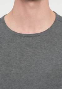 Sivi pulover z okrolim izrezom iz mehke, teksturirane pletene tkanine. Ima čist zaključek okoli izreza brez vidnih vzorcev ali poudarkov.