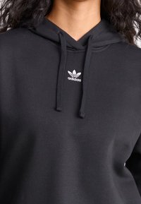 Felpa nera con cappuccio in tessuto morbido, caratterizzata da un piccolo logo Adidas bianco sul petto e da coulisse sul cappuccio.