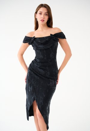 Abito nero off-shoulder con scollatura drappeggiata, corpino strutturato, tessuto testurizzato e una fessura alta fino alla coscia su un lato.