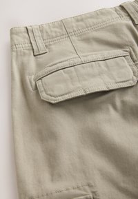 Pantalon cargo en coton beige avec une poche à rabat à l'arrière, des passants pour ceinture et des détails de couture visibles, présentant une texture lisse et un design décontracté.