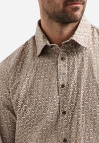 Lichtbeige overhemd met een geometrisch patroon van bruine en groene ovalen, voorzien van een klassieke kraag en donkere knopen.
