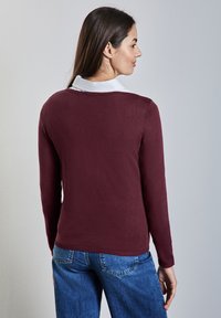 Pull en maille bordeaux avec manches longues et col blanc, présentant un encolure arrondie et une bordure ajustée, vu de dos.