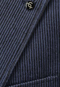 Marineblauer Cord-Stoff mit vertikalen Streifen, ausgestattet mit einem schwarzen Knopf mit Logo und einem strukturierten Kragen-Detail.