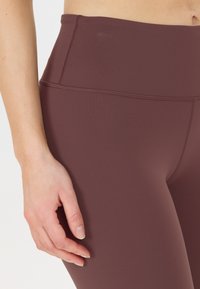 Högmidjade bordeaux leggings gjorda av stretchigt material, med en mjuk yta och detaljerad sömnad längs sömmarna.