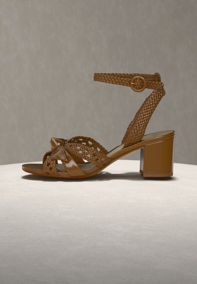 Καφέ δερμάτινο σανδάλι με τακούνι σε σχήμα μπλοκ, πλεγμένα λουριά, λουράκι αστραγάλου με κυκλική πόρπη και ανοιχτό σχέδιο δακτύλων σε ουδέτερη επιφάνεια.