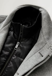 Grijs houndstooth-jack met een zwarte voering en kraag met rits. De stof heeft een gestructureerd patroon en geklede details.