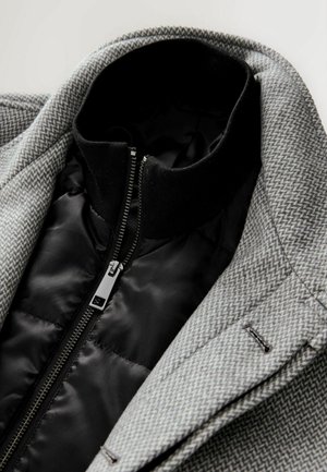 Grijs houndstooth-jack met een zwarte voering en kraag met rits. De stof heeft een gestructureerd patroon en geklede details.