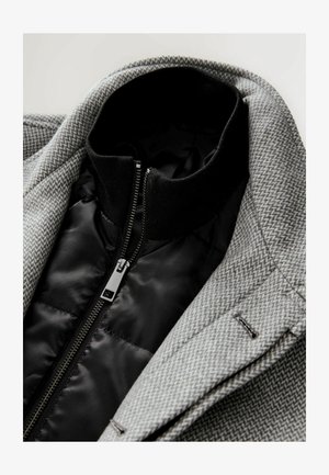 Gray houndstooth jacket featuring a black inner lining and collar with a zipper. The fabric has a textured pattern and tailored details.