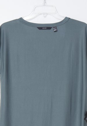 Loe fit teal T-särk ümmarguse kaelusega ja lühikeste varrukatega. Kangas näeb välja sile. Silt on nähtav selja kaeluses. Ei ole mustreid ega aksessuaare.