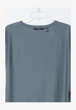 Loe fit teal T-särk ümmarguse kaelusega ja lühikeste varrukatega. Kangas näeb välja sile. Silt on nähtav selja kaeluses. Ei ole mustreid ega aksessuaare.