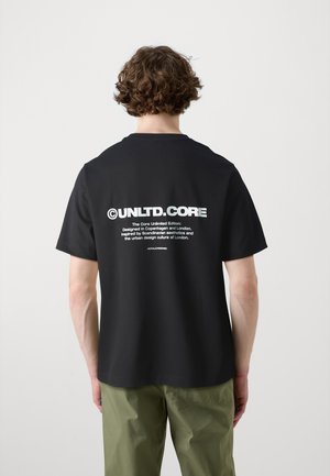 Czarny bawełniany t-shirt z okrągłym dekoltem, z wyraźnym białym napisem na plecach. Do tego luźne spodnie w kolorze oliwkowej zieleni.