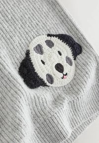 Tessuto a maglia grigio con un ricamo di una faccia di cane in bianco e nero, con caratteristiche facciali ben definite e un dettaglio della lingua rosa.