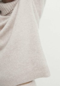 Ljusrosa stickad tröja med ribbat halsband och korta, lösa ärmar. Mjuk textur med ett subtilt fläckigt mönster.