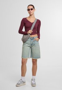 Top de manga larga burdeos, pantalones cortos de mezclilla azul claro, bolso de hombro acolchado gris, zapatillas gris y gafas de sol oscuras. Atuendo casual de verano.