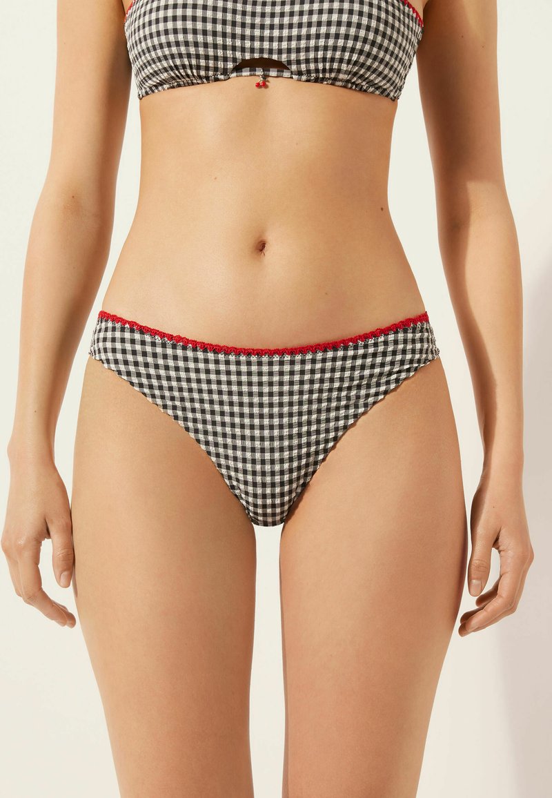 Svart och vit rutigt bikinitrosa med röda vågiga kanter. Har en medelhög skärning och en mjuk tygtextur.