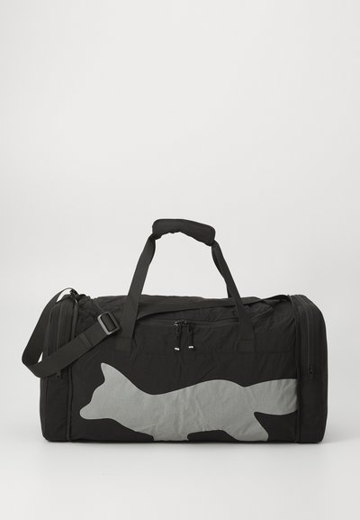 Musta duffel-laukku, joka on valmistettu kestävästä kankaasta, jossa on suuri harmaan ketun siluetti, kaksi kahvaa ja irrotettava olkahihna monipuoliseen kuljetukseen.
