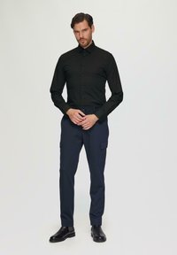Zwarte lange mouwen knoopshirt gecombineerd met marineblauwe cargobroek, met zakken en een getailleerd ontwerp. Zwarte leren enkellaarzen maken de outfit af.