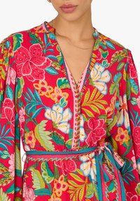 Florales Wickelkleid in lebendigem Rot mit grünen und pinken Akzenten. Verfügt über einen V-Ausschnitt, Knopfdetails und eine gebundene Taille, die das Blumenmuster betont.