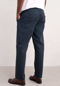 Pantaloni in cotone blu navy con gamba dritta, dotati di due tasche posteriori, tasche laterali e una texture liscia. Indossati con scarpe marroni.