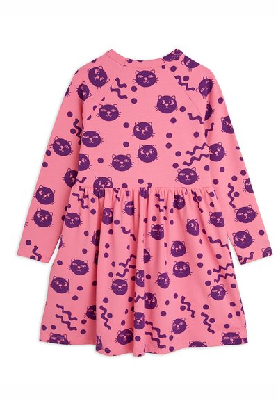 Long-sleeve dress in pink fabric featuring a pattern of purple cat faces and abstract shapes. Skirt has a gathered design.