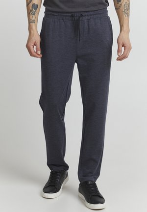 Dark gray sweatpants with an elastic waistband and drawstring, featuring side pockets and a tapered leg design, worn with black sneakers.