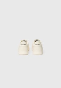 Fehér bőr sportcipők textúrázott nyelvvel és puha talppal. A sarkán "LACOSTE" logóval. Simító felület minimális díszítésekkel.