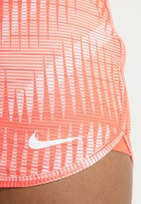 Pantalones cortos Nike en un brillante color coral con un patrón de rayas en degradado. Presentan un pequeño logotipo blanco y un ajuste ceñido con una textura de tela suave.