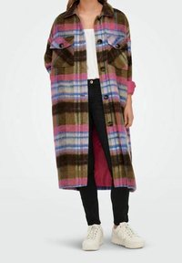 Long plaid coat in green, pink, blue, and brown over white top, black pants, and white sneakers on standing person.
