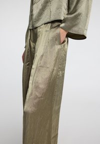Olive green, textured outfit featuring a loose top with three-quarter sleeves and wide-leg pants with side pockets. Smooth, flowing fabric.