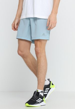 Hellblaue Sportshorts mit einem strukturierten Muster, kombiniert mit schwarzen und gelben Sportschuhen mit drei weißen Streifen.