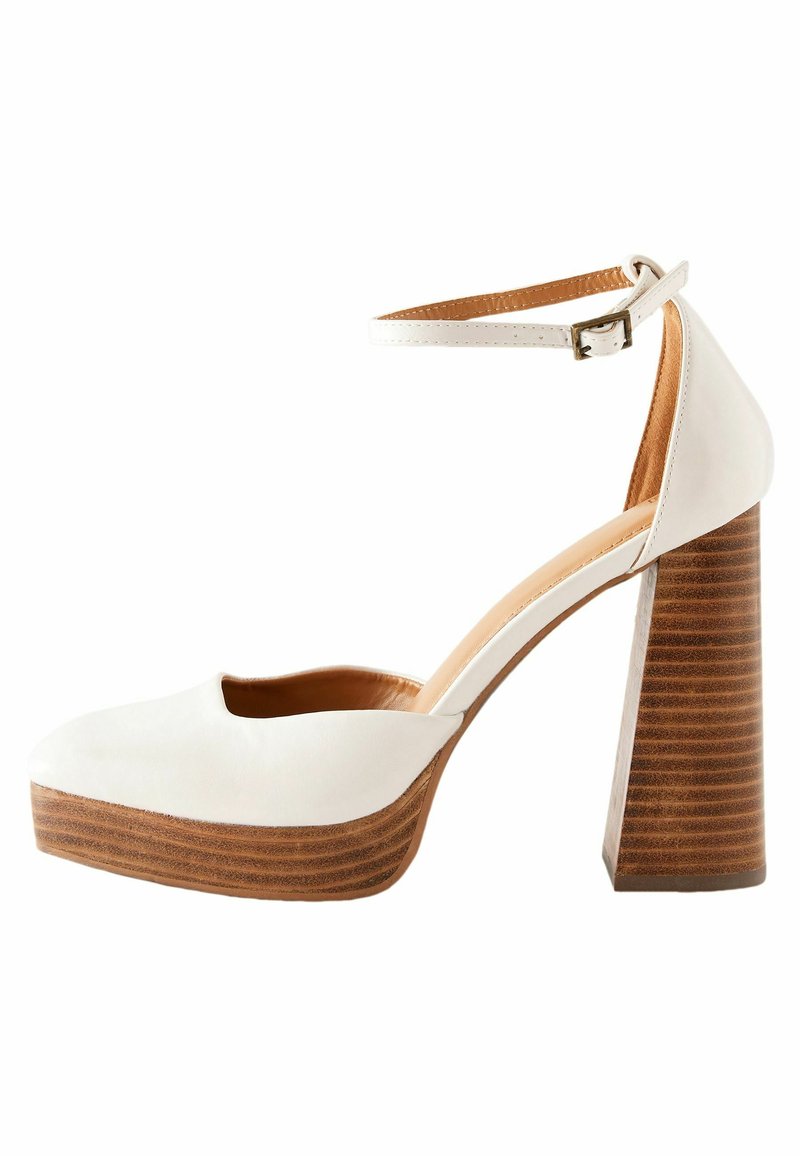 Escarpins compensés en cuir blanc avec un bout rond, une bride à la cheville et un talon bloc rayé marron. Texture lisse et design minimaliste.