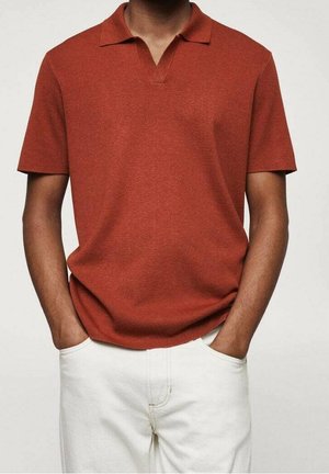 Krustfarbener Poloshirt mit V-Ausschnitt und kurzen Ärmeln. Hergestellt aus einem strukturierten Strickstoff. Getragen mit hellen Hosen.