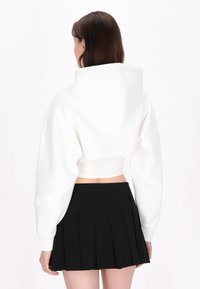 Biały krótki hoodie z dużym kapturem, z luźnymi rękawami. Połączony z czarną plisowaną mini spódnicą.