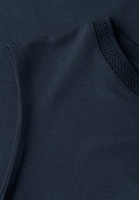 Gros plan sur un tissu en maille bleu foncé montrant la couture d'épaule et l'encolure côtelée texturée d'un vêtement sans manches.