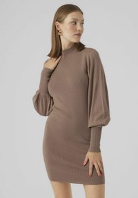 Abito lavorato a maglia in caldo taupe con collo alto, corpo aderente e maniche lunghe a sbuffo, che mostra una texture a coste. Senza motivi o accenti notevoli.