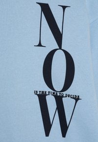 Ljusblå tygtröja med kraftig svart text: "NU ÄR DET DAGS ATT BESTÄMMA," i ett modernt typsnitt och minimalistisk design.