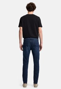 Mörkblå denimjeans med slim fit, mid-rise midja och två bakfickor. Bärs med en svart t-shirt och ljusa skor.